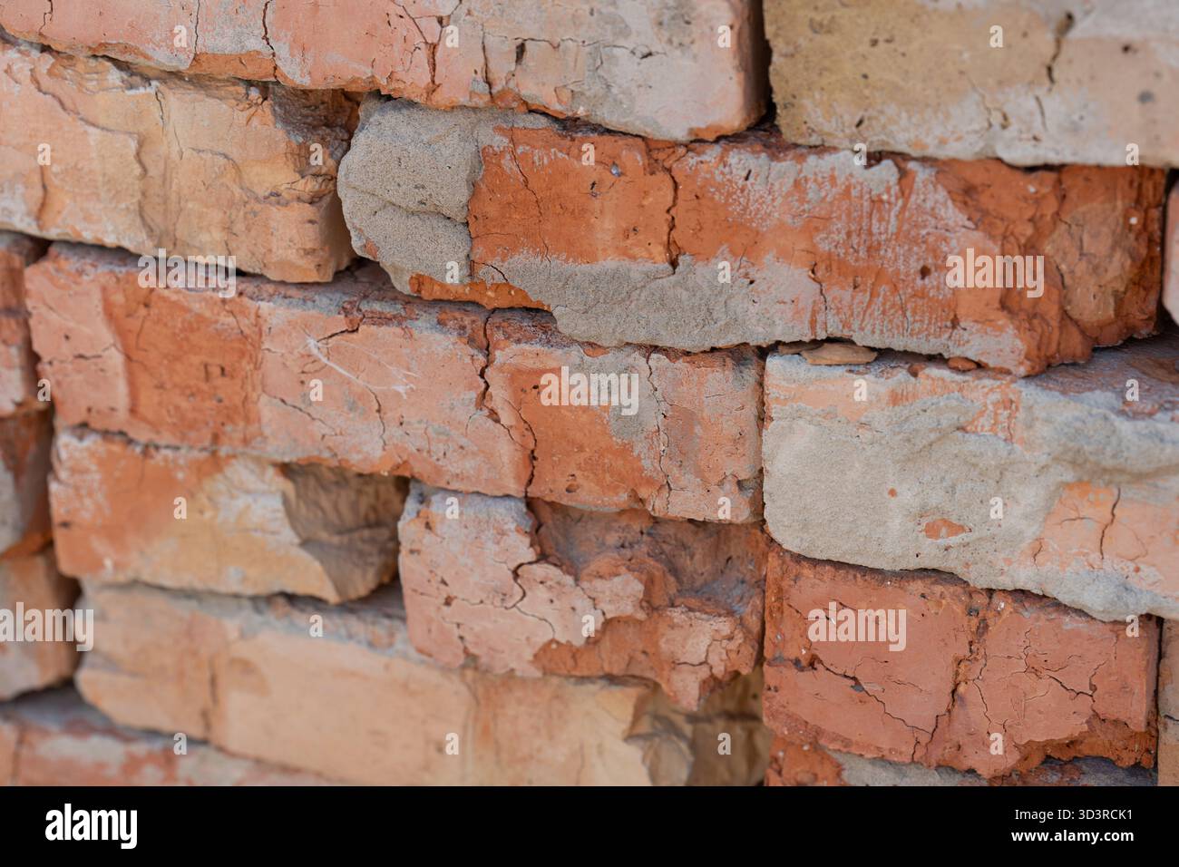 Des briques robustes dans des tons rouges et oranges variés forment une pile murale altérée. Les surfaces fissurées, le mortier exposé, la texture rugueuse transmettent la durabilité, l'histoire, l'esthétique de construction rustique Banque D'Images