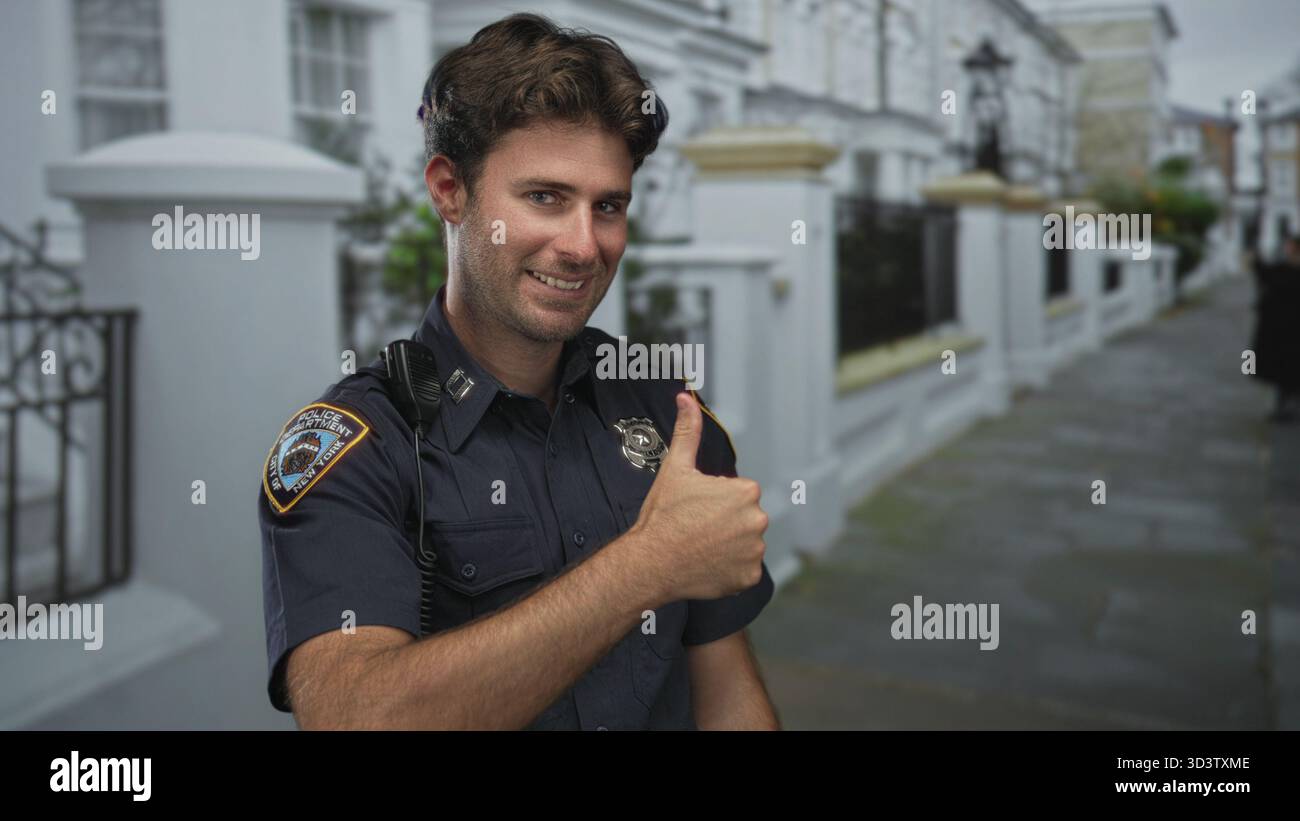 Homme policier souriant et donnant les pouces dans la rue portant uniforme, badge et radio d'épaule ; confiance de la communauté. Banque D'Images