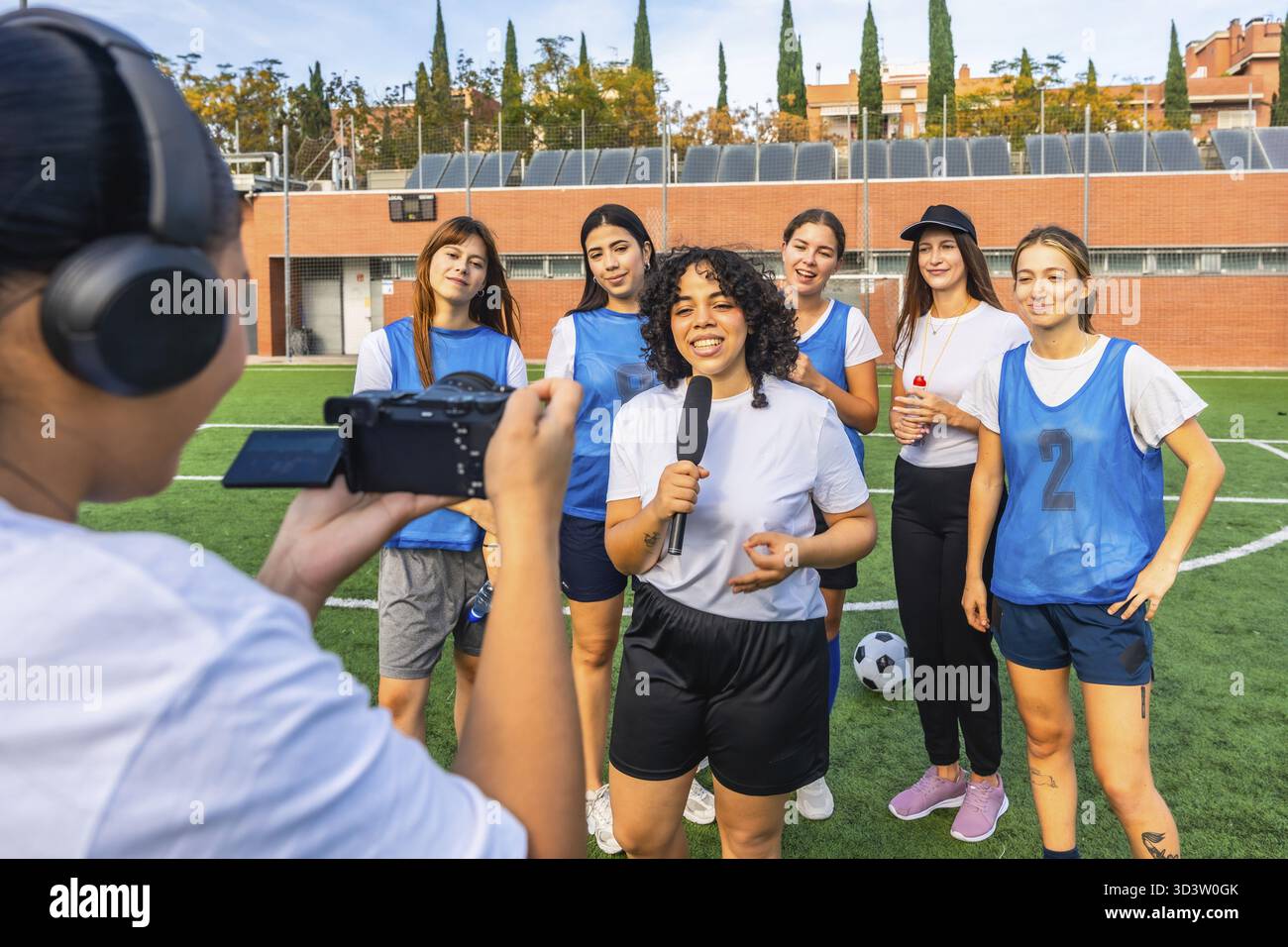 Journaliste sportive féminine interviewe une équipe de soccer féminine diversifiée sur un terrain vert, capturant leurs histoires et expériences après une séance d'entraînement Banque D'Images