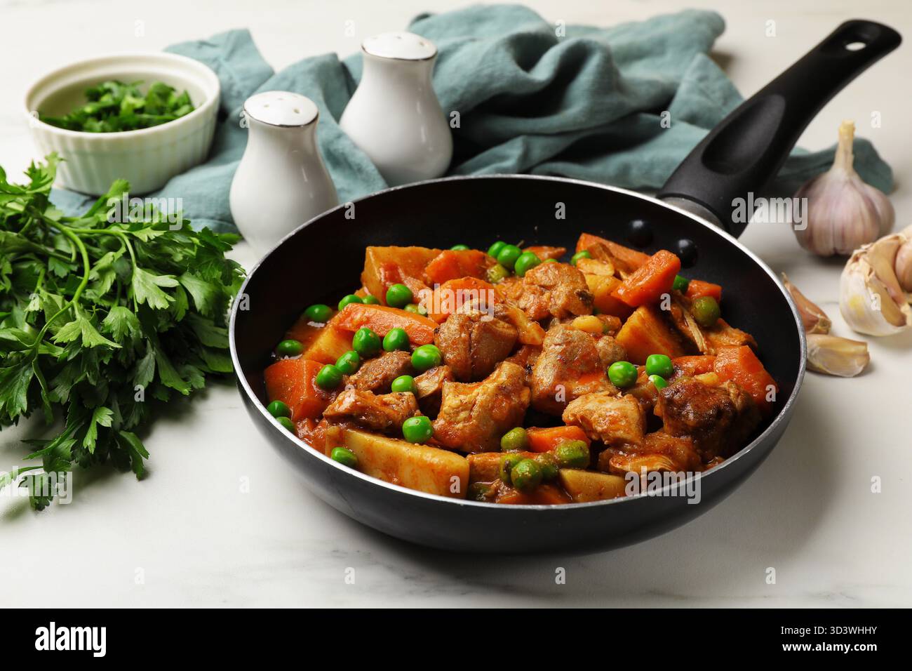 Délicieux ragoût cuit dans une poêle, persil et ail sur une table en marbre blanc, gros plan Banque D'Images