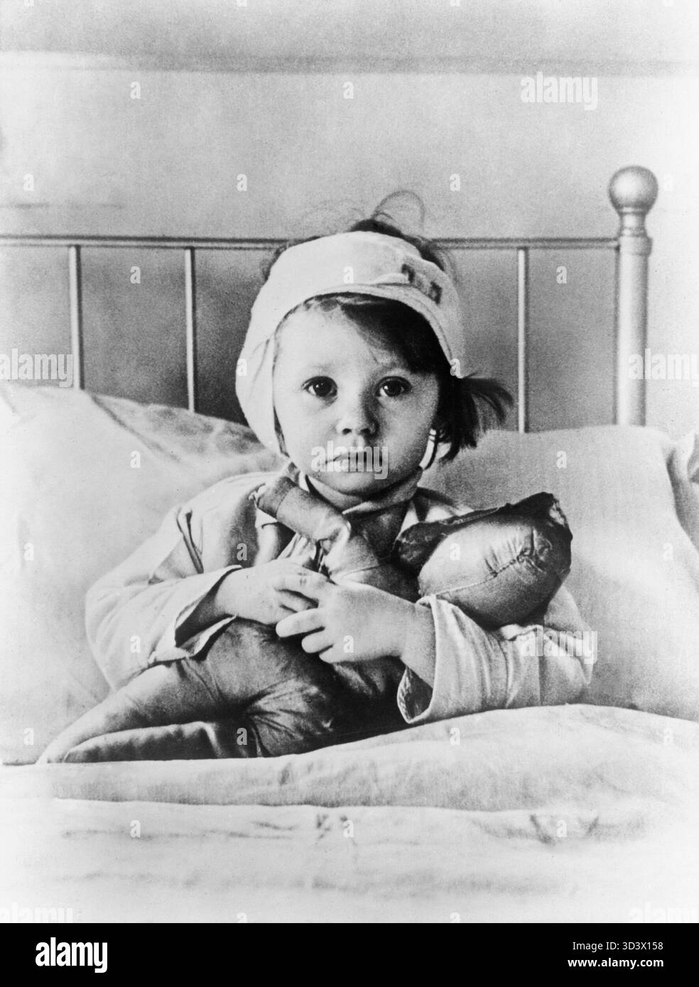 The London Blitz, tirage d'exposition vintage des années 1940 1940 de la photographie de Cecil Beaton Eileen Dunne, trois ans, est assise au lit avec sa poupée au Great Ormond Street Hospital for Sick Children, après avoir été blessée lors d'un raid aérien sur Londres en septembre 1940. Banque D'Images