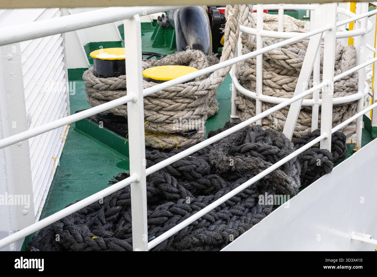 Une scène maritime avec des bobines de corde épaisses sur un pont de navire vert, des garde-corps blancs et des bornes jaune vif. L'arrangement transporte le travail nautique, s Banque D'Images