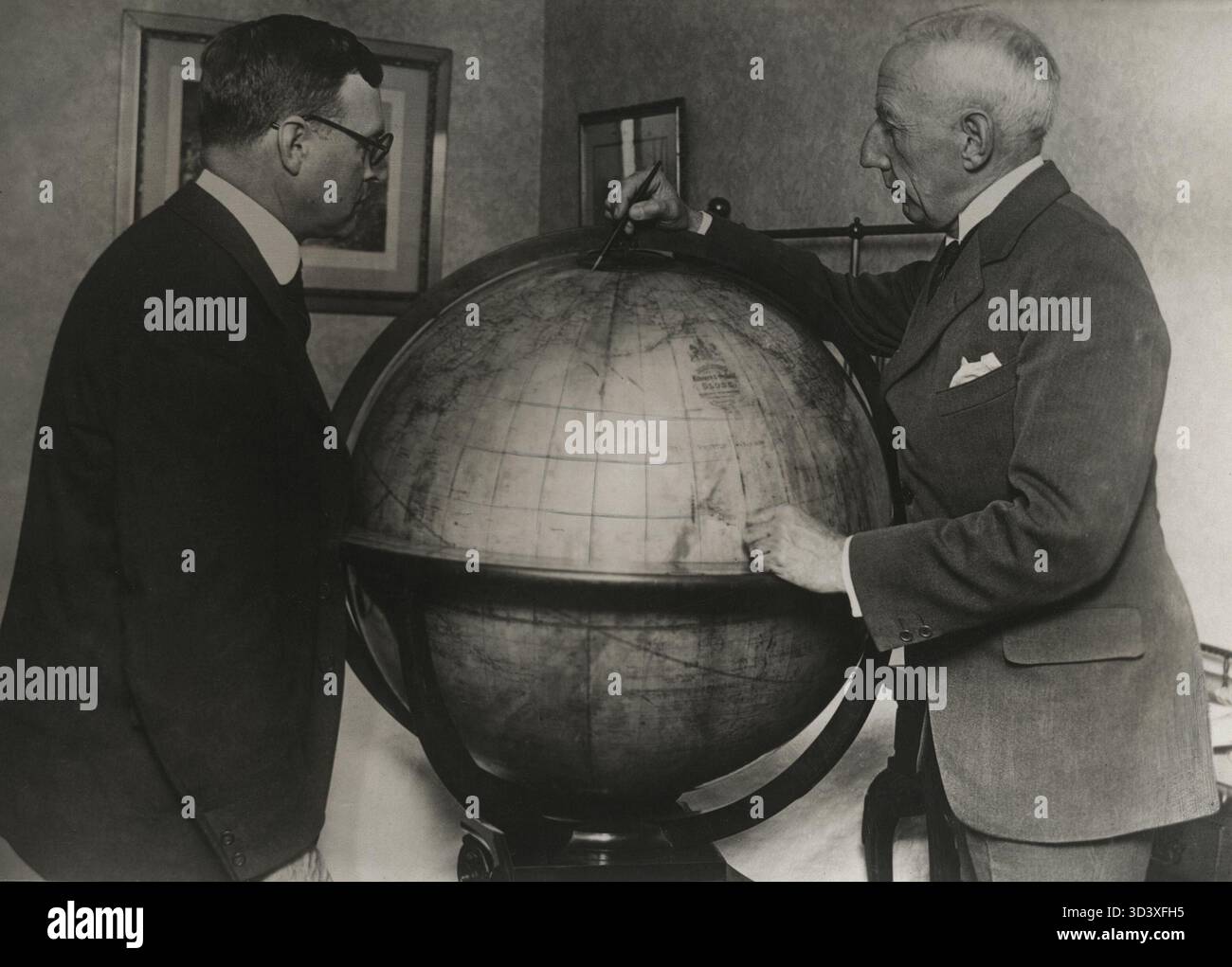 Roald Amundsen (à droite) se tient à côté d'un globe, pointant vers le pôle Nord. La photo a été prise peu avant son départ en 1925. Amundsen était un explorateur polaire de premier plan. Banque D'Images