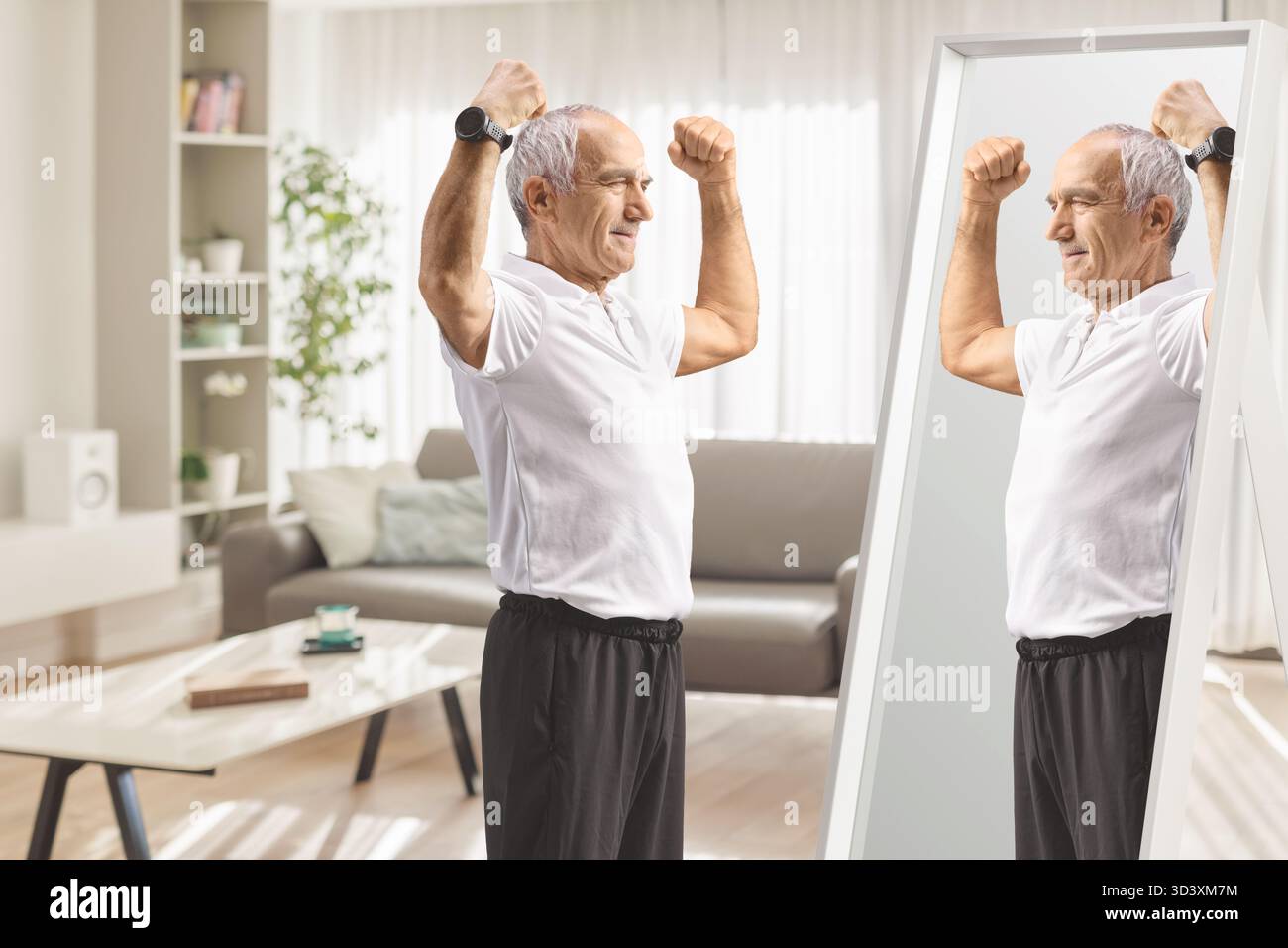 Senior en vêtements de sport fléchissant les muscles du bras devant le miroir à la maison Banque D'Images