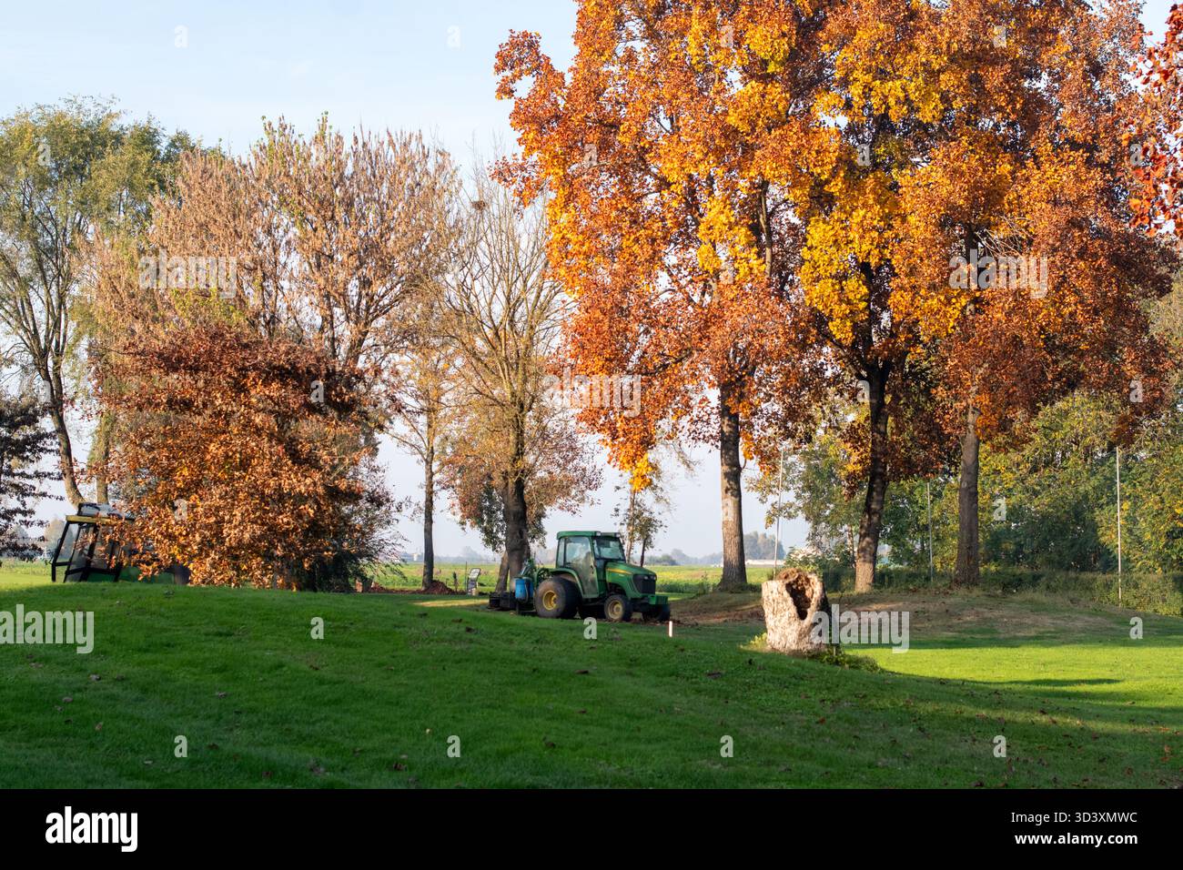 Green John Deere tracteur garé sur une colline herbeuse à côté d'arbres d'automne vibrants, scène de campagne rurale Banque D'Images