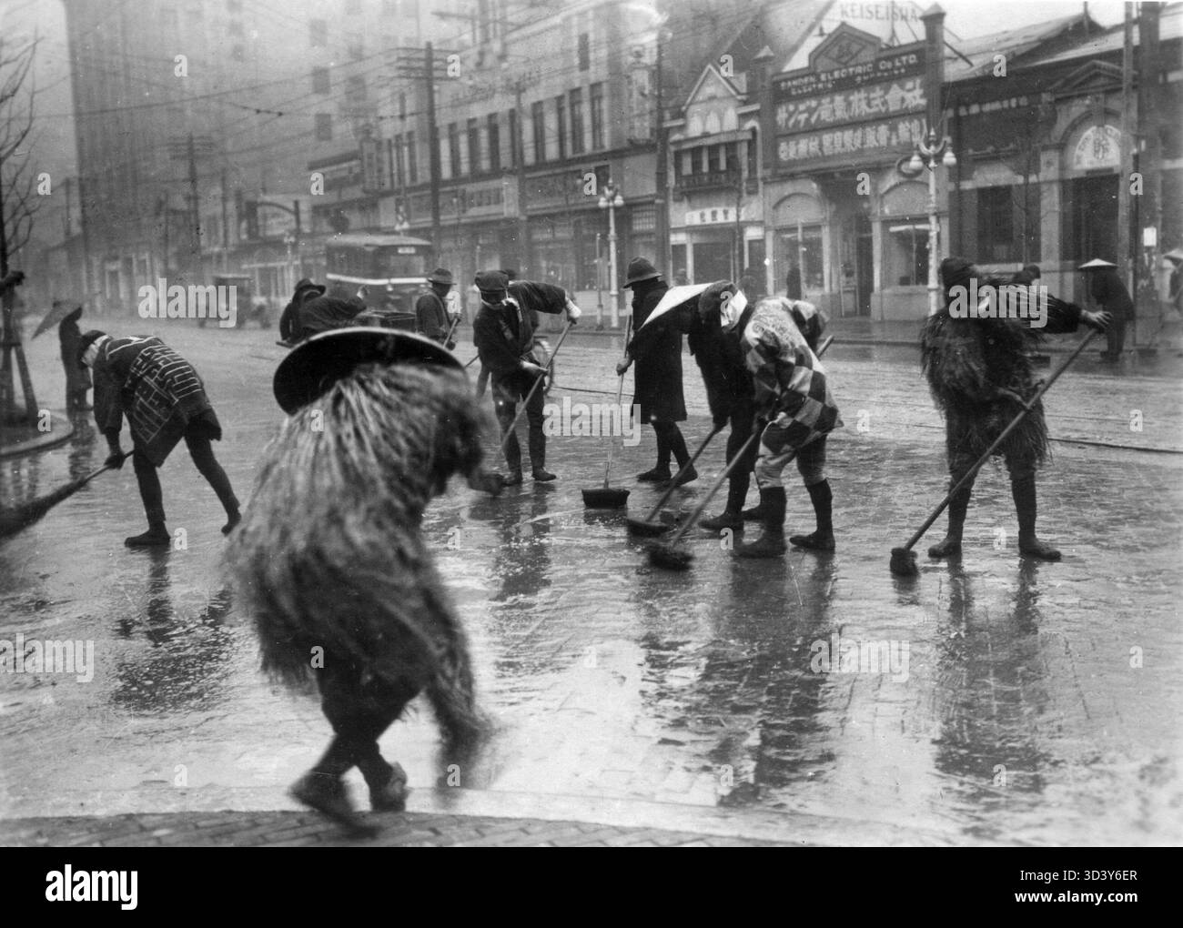 Une scène de rue lors d'une tempête à Tokyo, Japon, entre 1928 et 1935. Malgré les fortes pluies, la rue est balayée avec des balais, mettant en valeur la vie quotidienne dans des conditions météorologiques difficiles. Banque D'Images