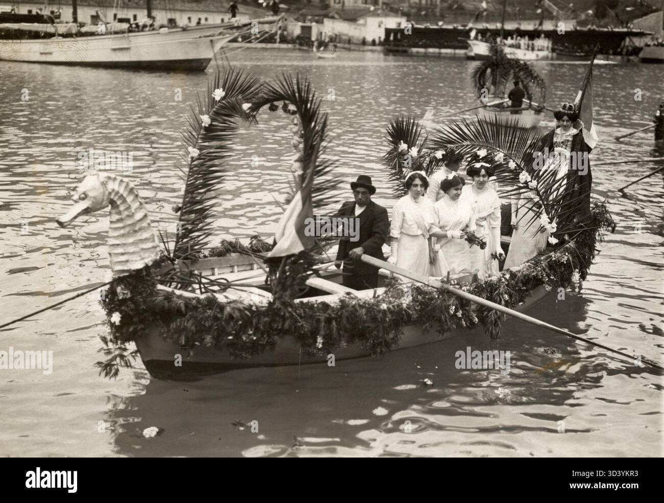 Un bateau à rames richement orné de fleurs participe au défilé fleuri de Venise de 1912. Le bateau présente un arc en forme de dragon et une figure reine à la poupe, reflétant le style grandiose des festivités florales aquatiques de Venise. Banque D'Images