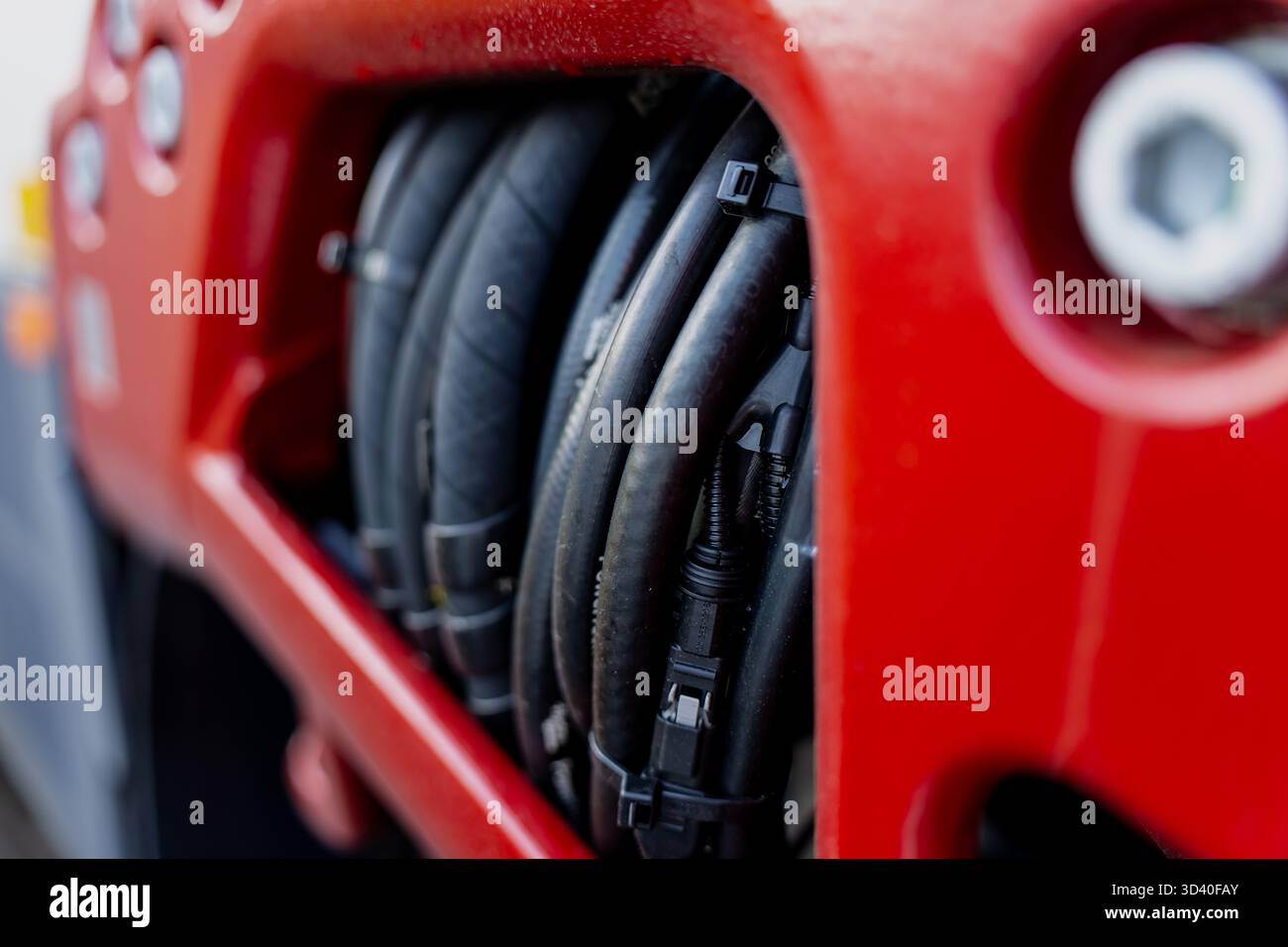Boîtier de machines en métal rouge avec flexibles hydrauliques groupés représentant la conception industrielle, l'ingénierie de l'énergie des fluides et la maintenance de l'équipement de construction Banque D'Images