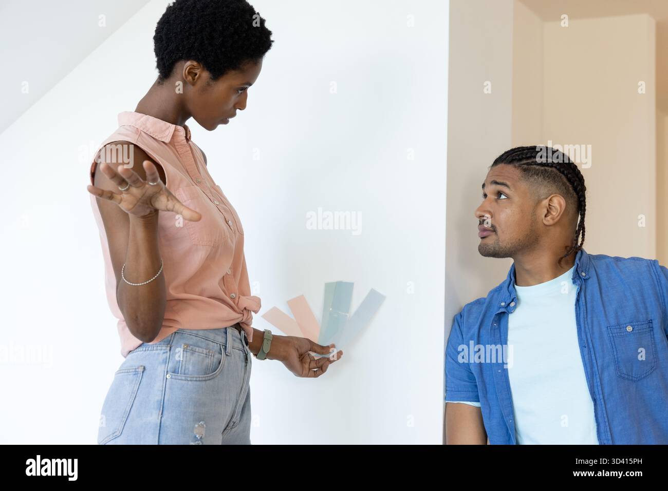 Couple diversifié sélectionnant des échantillons de peinture dans une pièce intérieure lumineuse, tenant des cartes de couleur pastel Banque D'Images