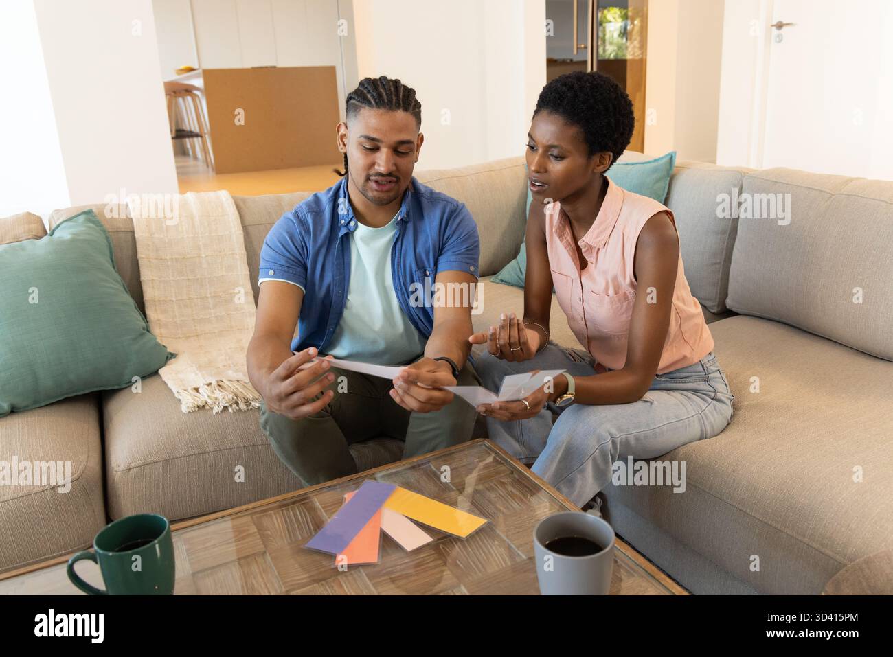Choisir des échantillons de couleur de peinture, couple diversifié assis sur un canapé dans un salon moderne avec des tasses à café Banque D'Images
