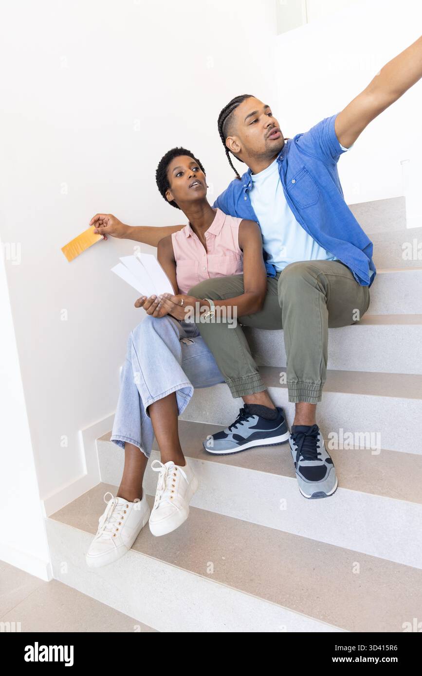 Pointant divers couples choisissant des échantillons de couleur de peinture sur l'escalier de la maison, tenant l'échantillon orange Banque D'Images