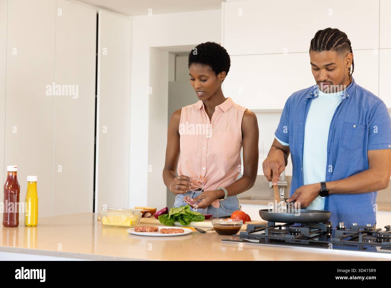 Cuisson de divers couples remuant la poêle à frire et hachant les épinards dans la cuisine maison, avec des saucisses Banque D'Images