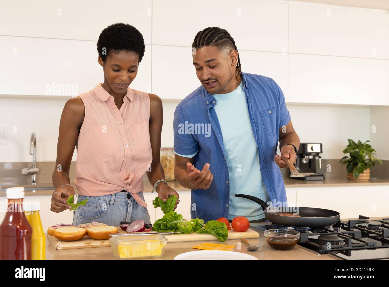 Cuisiner divers couples hachant de la laitue et griller des hamburgers au comptoir de la cuisine, avec une spatule Banque D'Images