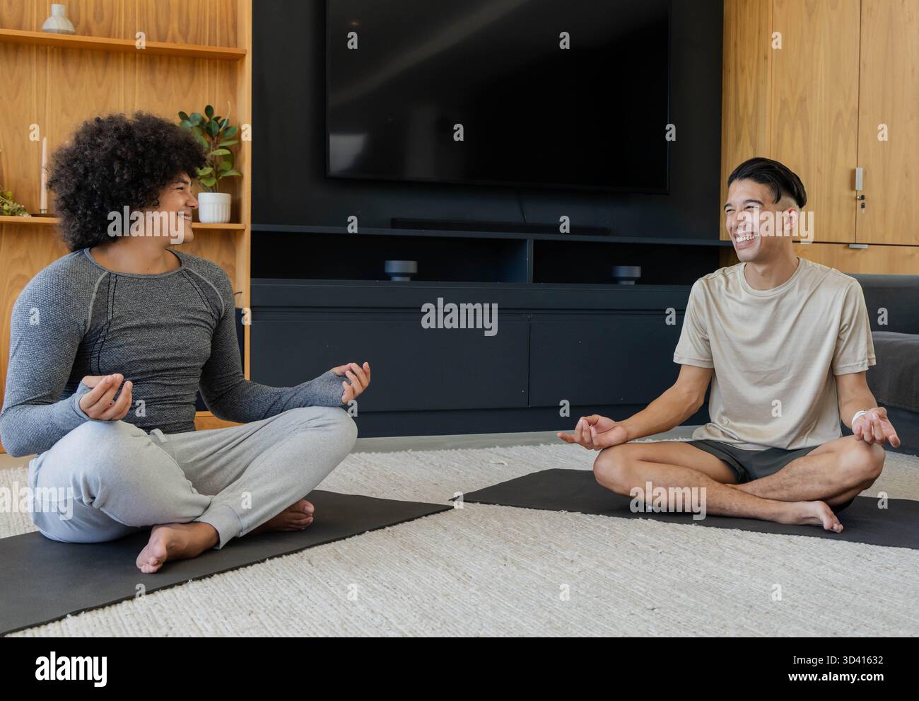 Divers amis masculins méditant dans le salon moderne sur tapis, avec tapis de yoga et télévision à écran plat Banque D'Images
