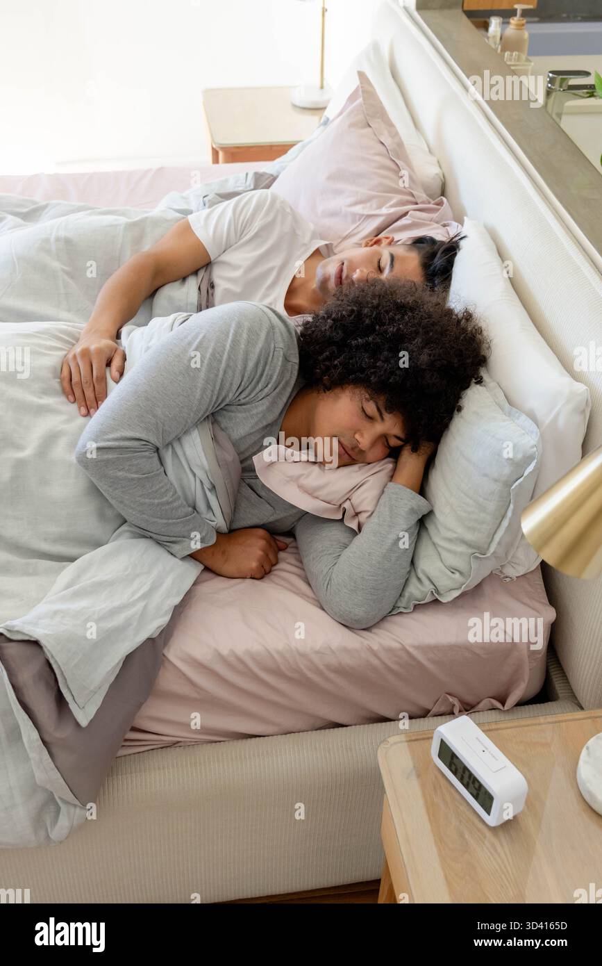 Couchage de deux hommes cuillère sur le lit dans une chambre moderne, avec réveil numérique et lampe Banque D'Images