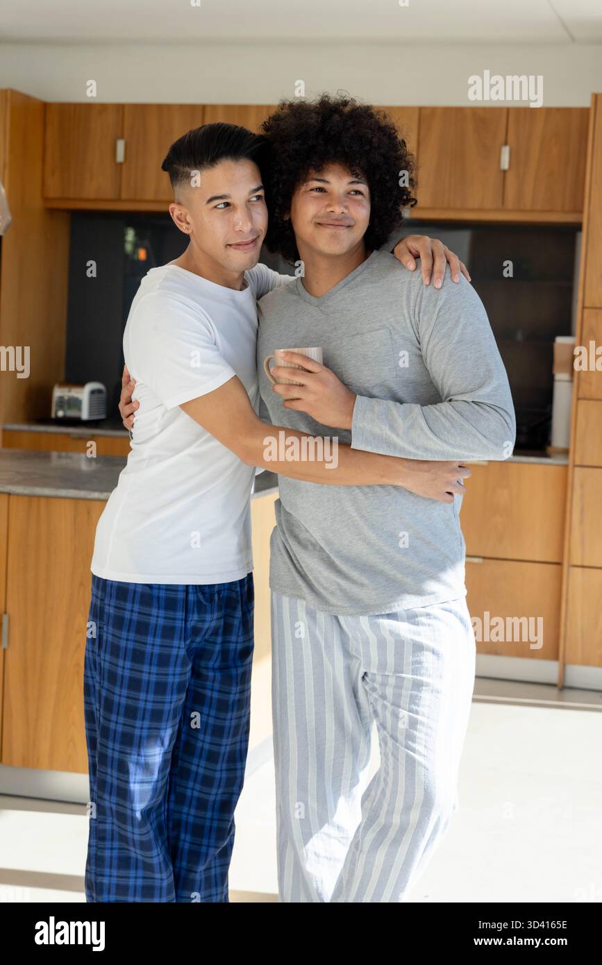 Embrasser deux hommes debout dans la cuisine moderne, avec tasse à café et grille-pain de comptoir Banque D'Images