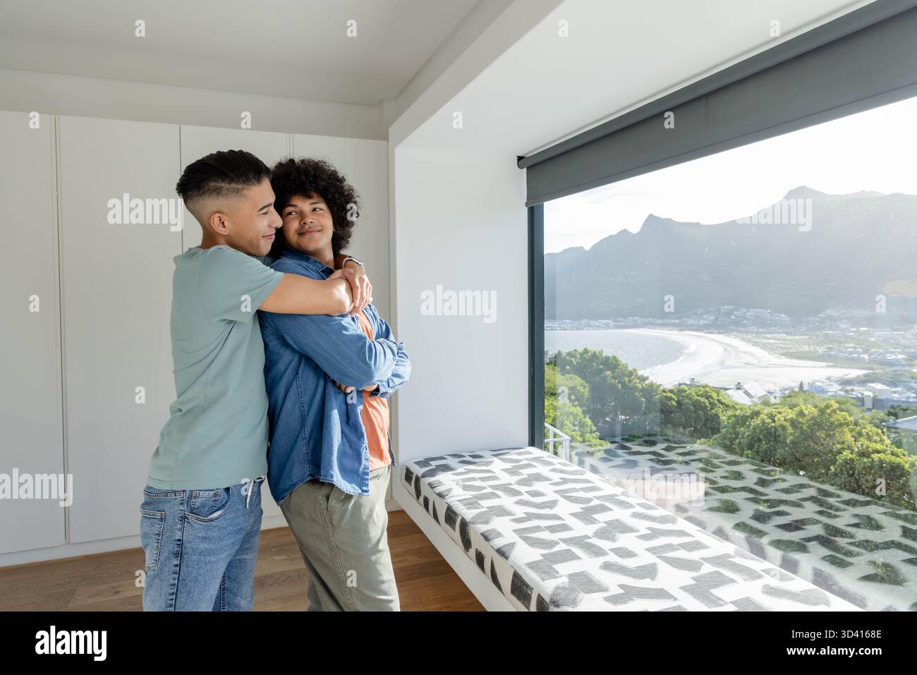 Embrasser divers partenaires masculins debout dans la maison côtière moderne avec fenêtre panoramique, espace de copie Banque D'Images