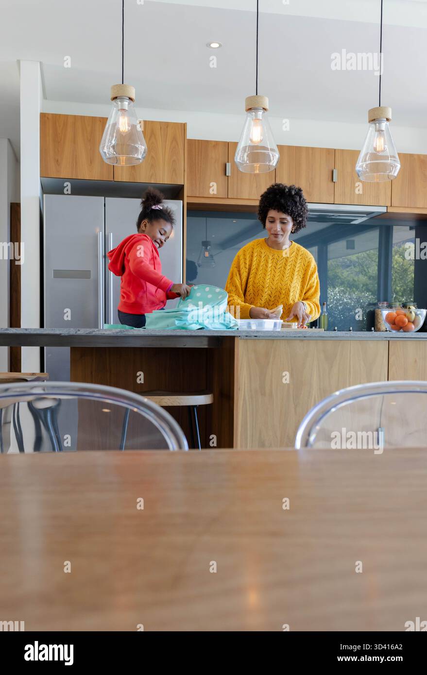 Mère et fille diversifiées emballant le déjeuner dans la cuisine moderne, avec sac à lunch sarcelle Banque D'Images