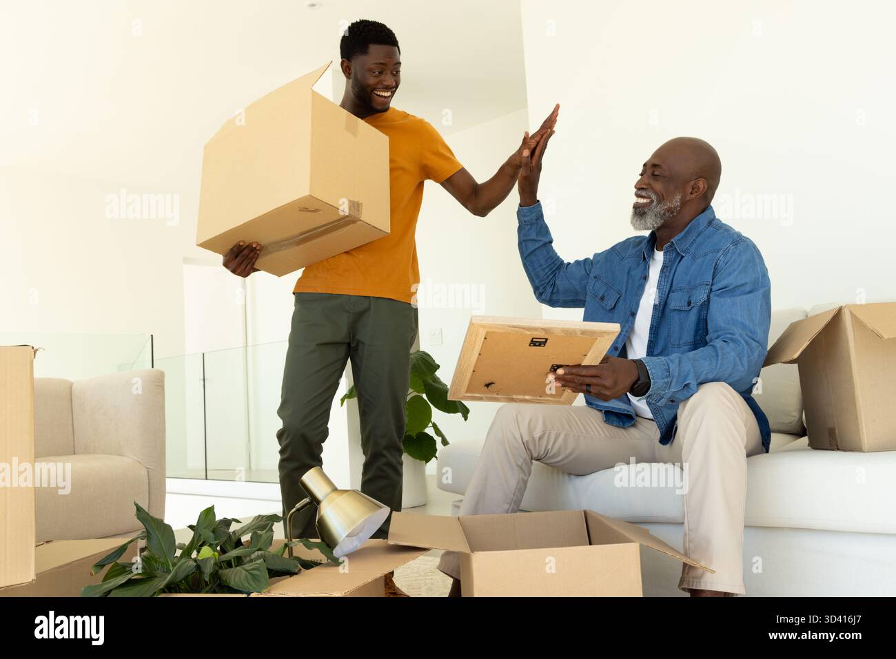 Père afro-américain et fils déballant des boîtes dans le salon, avec cadre photo Banque D'Images