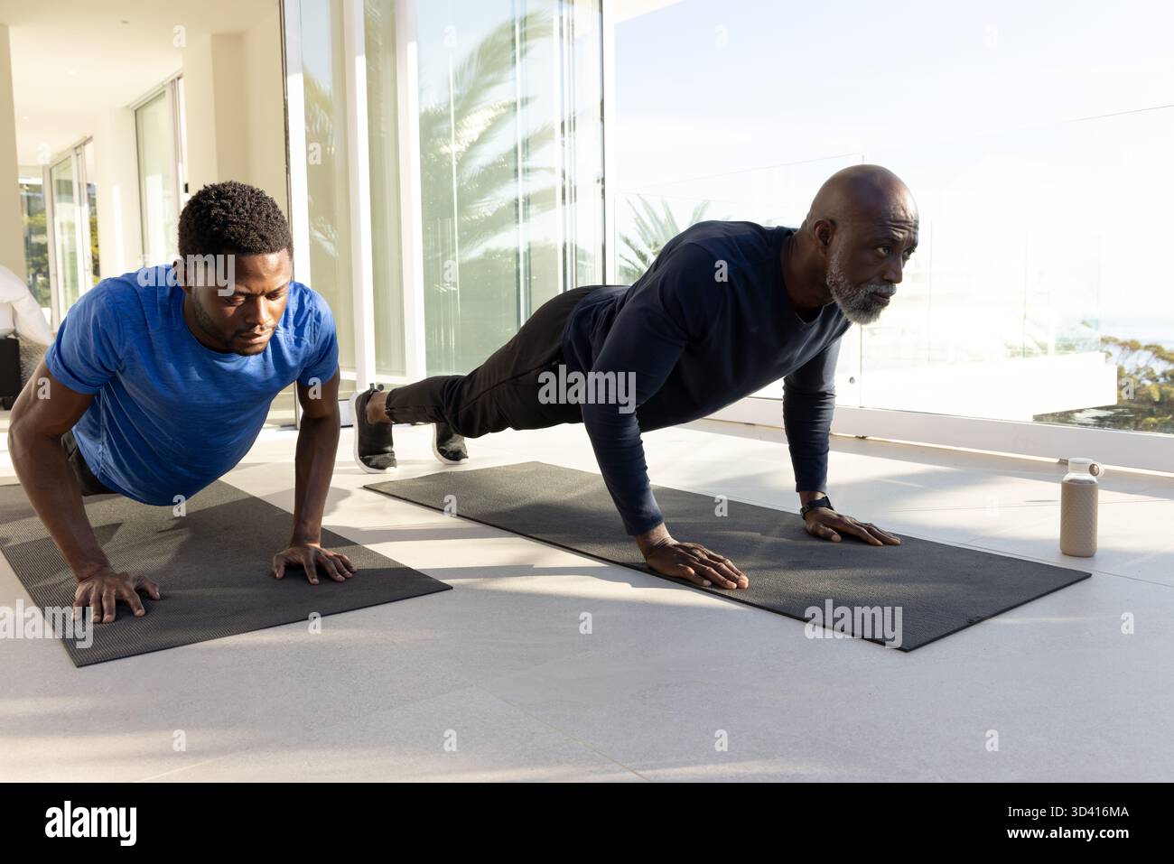 Exécution de pompes afro-américaines père et fils sur des tapis noirs dans la chambre, avec bouteille d'eau beige Banque D'Images