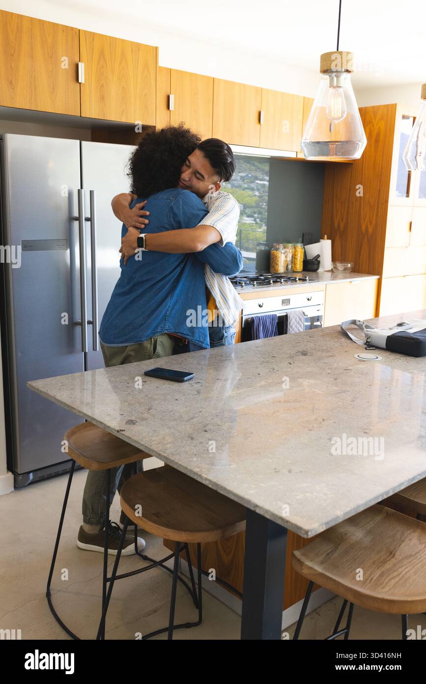 Embrasser divers hommes debout près de l'île de marbre dans la cuisine moderne, avec smartphone, espace de copie Banque D'Images