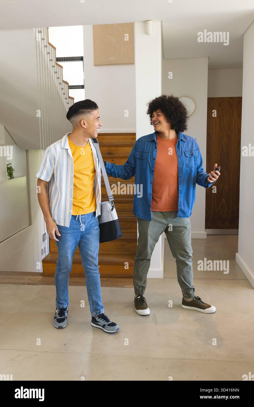 Divers amis masculins discutant dans l'entrée par escalier, avec sac à bandoulière et smartphone Banque D'Images