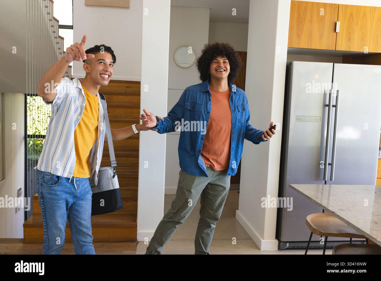 Accueillant divers amis masculins faisant des gestes dans l'entrée de la maison, avec sac à bandoulière et smartphone Banque D'Images