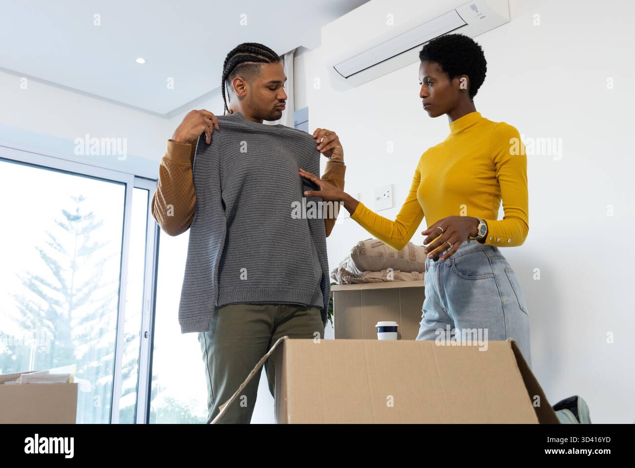Déballage de divers couples inspectant le pull gris dans le salon, avec des boîtes et une tasse à café Banque D'Images