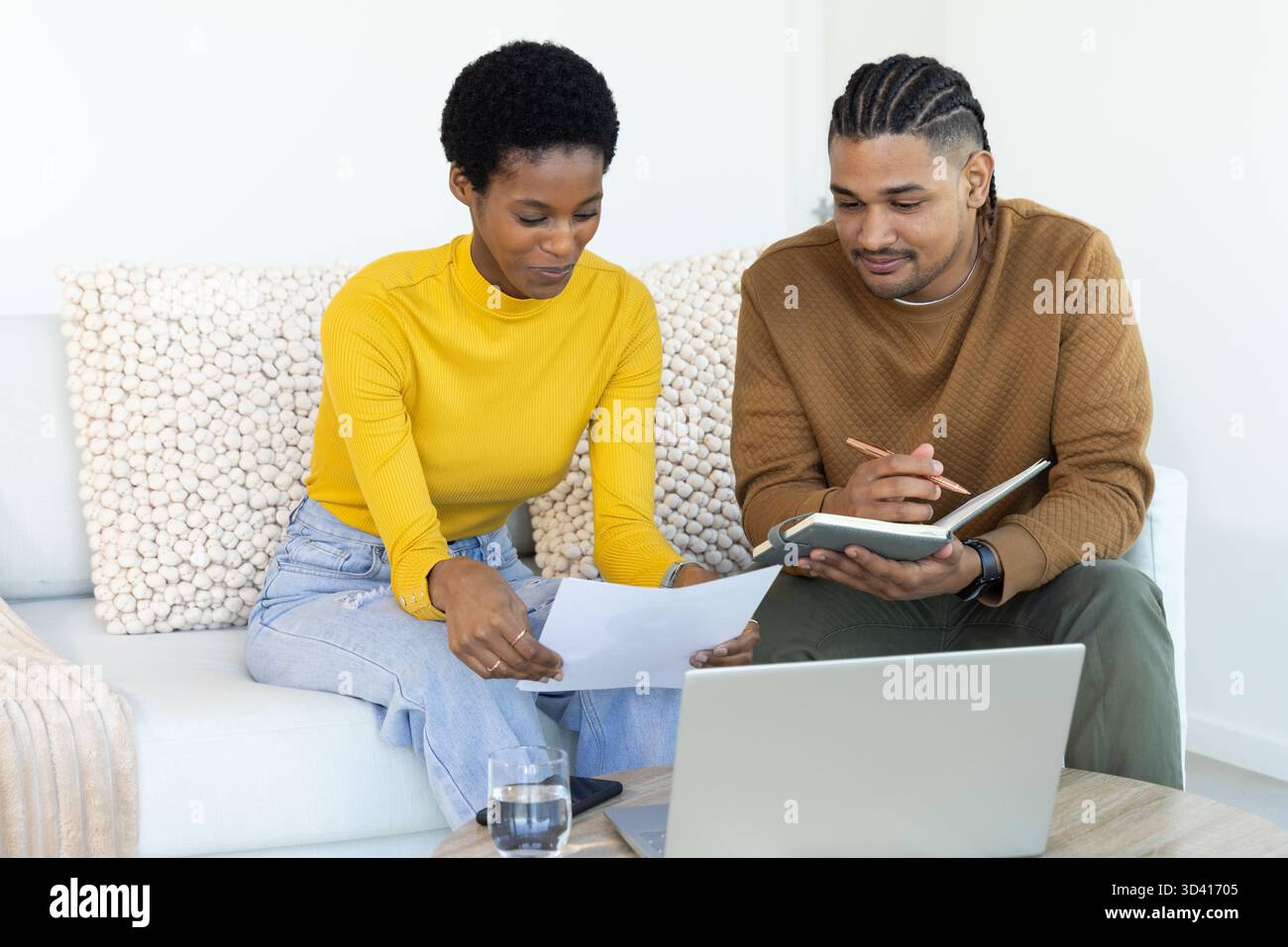 Couple diversifié examinant des documents et ordinateur portable sur canapé dans le salon, avec smartphone Banque D'Images