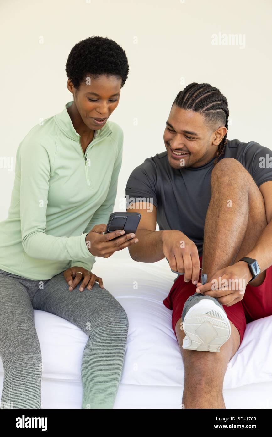 Montrant divers amis assis sur le lit dans la chambre, avec smartphone, smartwatch et baskets blanches Banque D'Images