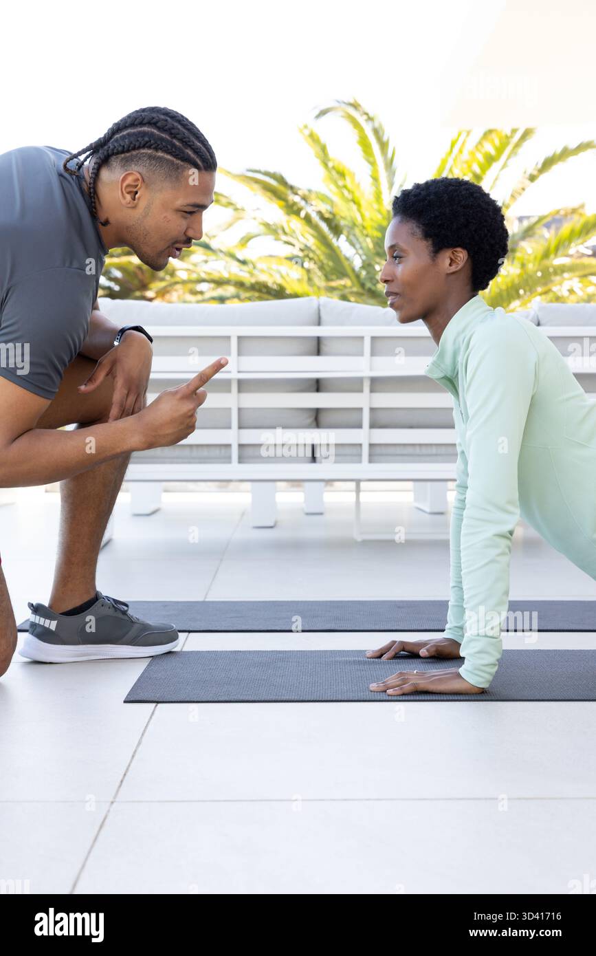 Exercice divers duo de fitness effectuant une séance d'entraînement sur la terrasse sur le toit, avec des tapis de yoga et smartwatch Banque D'Images