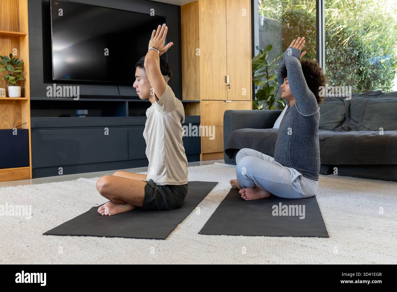 Étirer divers amis masculins tenant la pose de yoga dans le salon avec des tapis de yoga noirs Banque D'Images