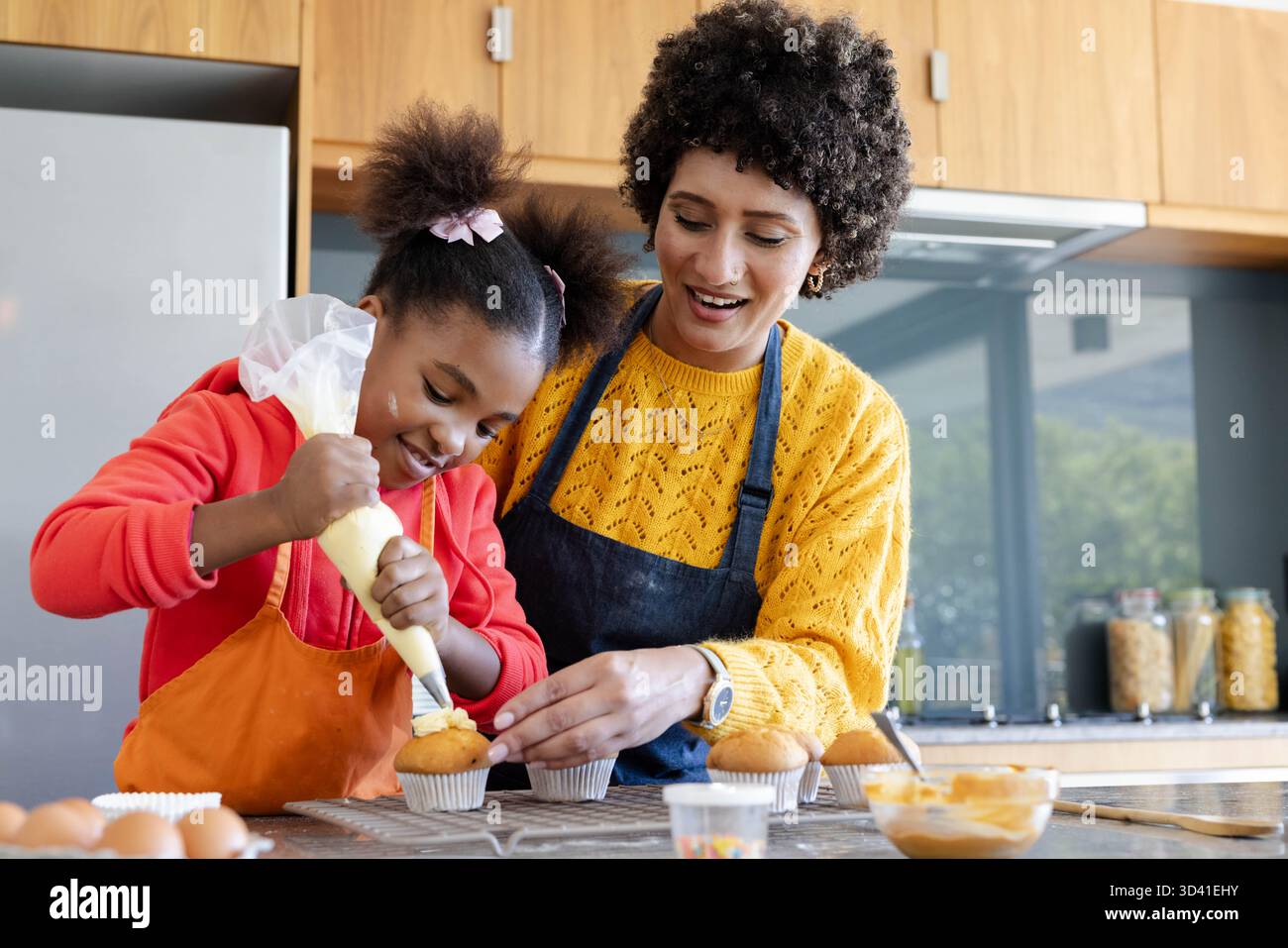 Mère et fille afro-américaine de passepoil glaçage sur les cupcakes à l'aide du sac à passepoil dans la cuisine Banque D'Images
