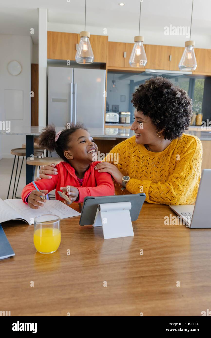 Encourager la mère et la fille diversifiées étudiant à la table de cuisine moderne, avec ordinateur portable et tablette Banque D'Images
