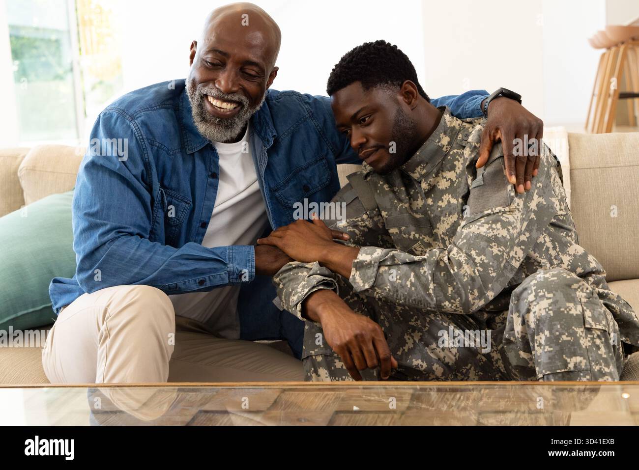 Réconfortant père afro-américain et fils assis sur le canapé dans le salon, avec uniforme de camouflage Banque D'Images