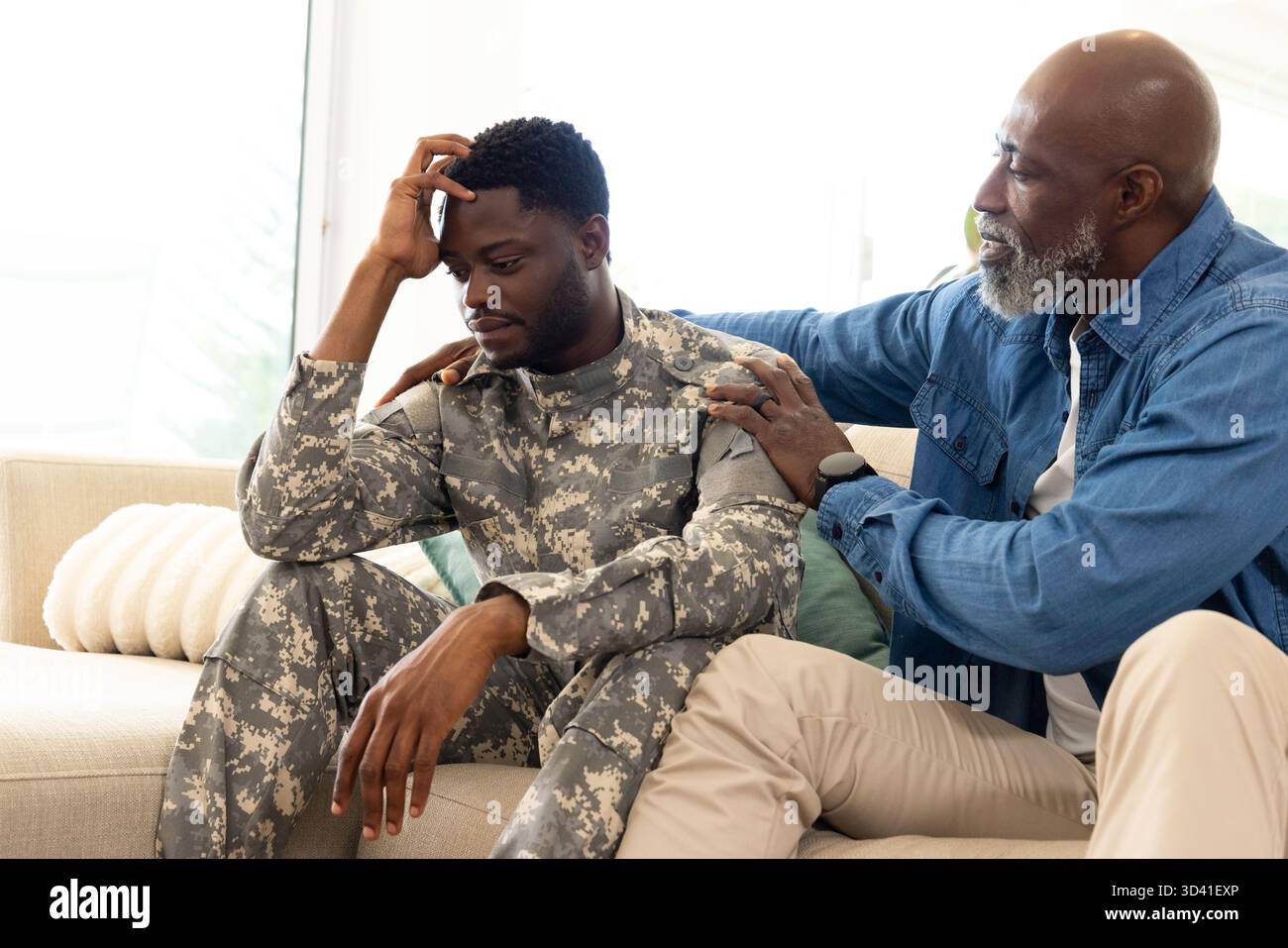 Père afro-américain et fils partageant moment à la maison sur le canapé, avec uniforme camouflage, espace copie Banque D'Images