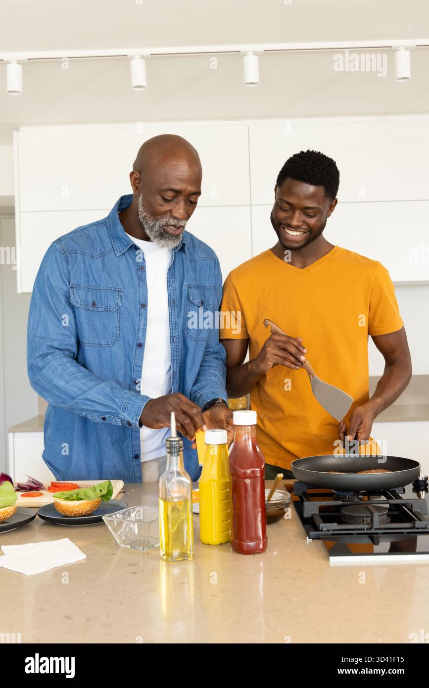 Famille afro-américaine préparant des petits pains et retournant des galettes au comptoir de cuisine, avec des condiments Banque D'Images