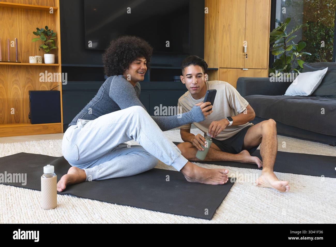Vérification smartphone divers amis masculins assis sur des tapis de yoga dans le salon, avec des bouteilles d'eau Banque D'Images