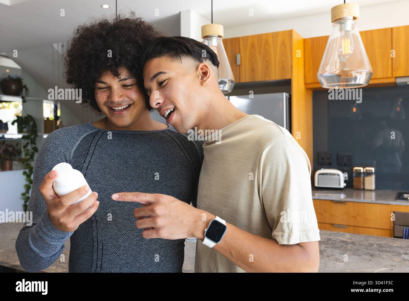 Tenant la bouteille en plastique, divers amis masculins examinant l'étiquette dans la cuisine, avec des lumières suspendues en verre Banque D'Images