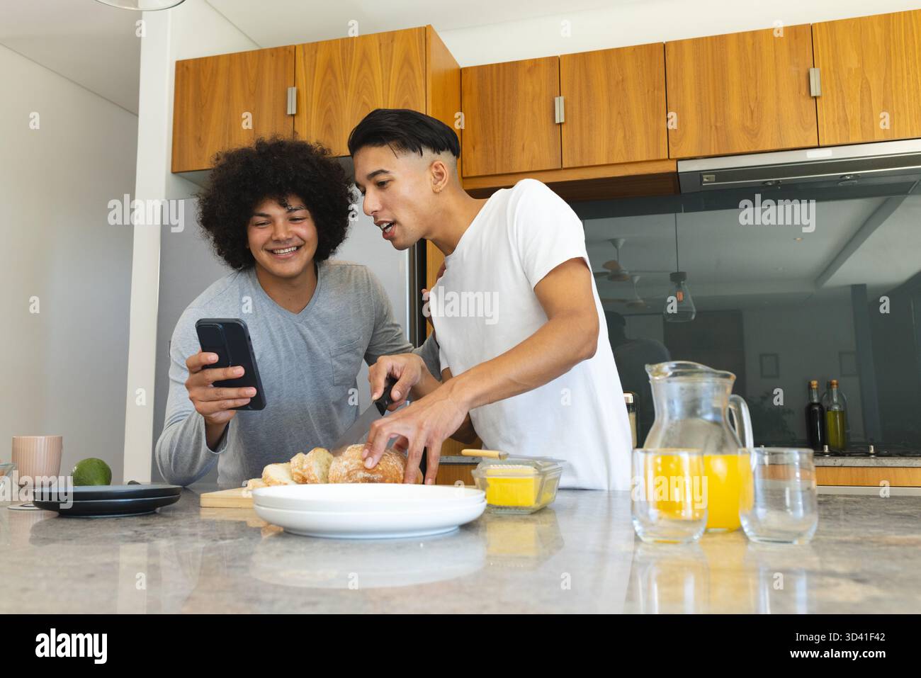 Trancher des croissants divers amis masculins vérifiant smartphone sur l'île de marbre, avec tasse et jus Banque D'Images