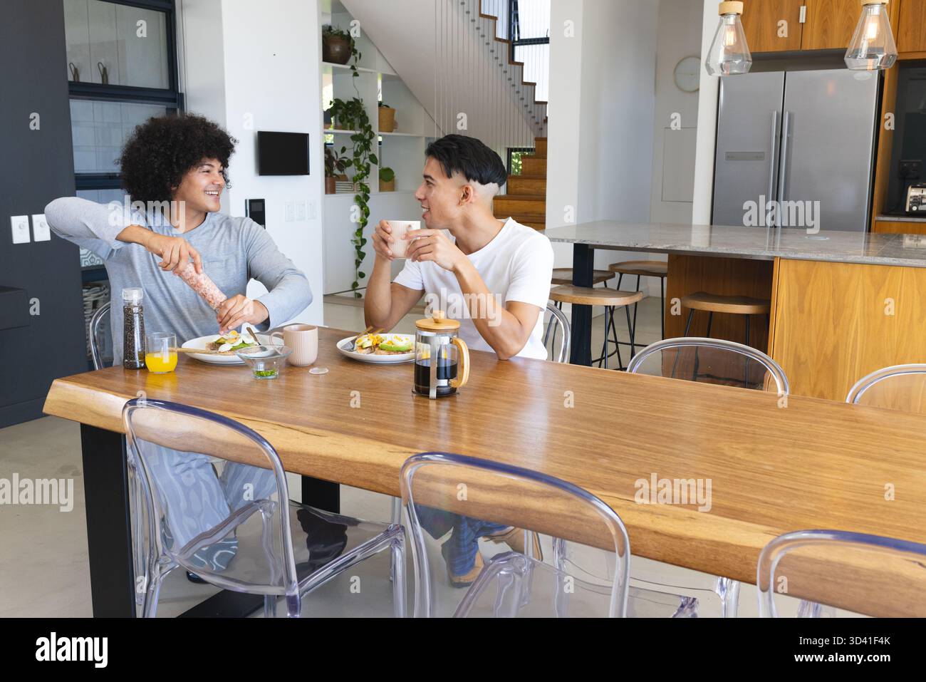 Divers amis masculins broyant du poivre sur un toast d'avocat à la table à manger de la cuisine, avec une tasse à café Banque D'Images