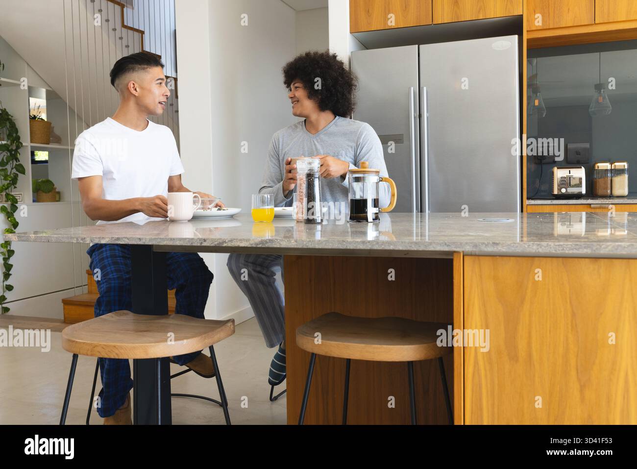 Deux hommes assis sur des tabourets à l'îlot de cuisine en marbre, partageant café et jus avec la presse française Banque D'Images