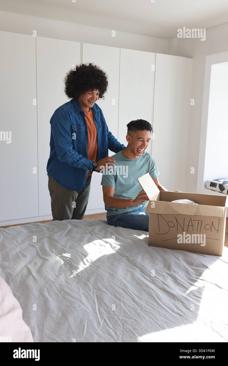 Emballer divers père et fils triant les articles de don sur le lit dans la chambre à coucher, avec boîte de don Banque D'Images