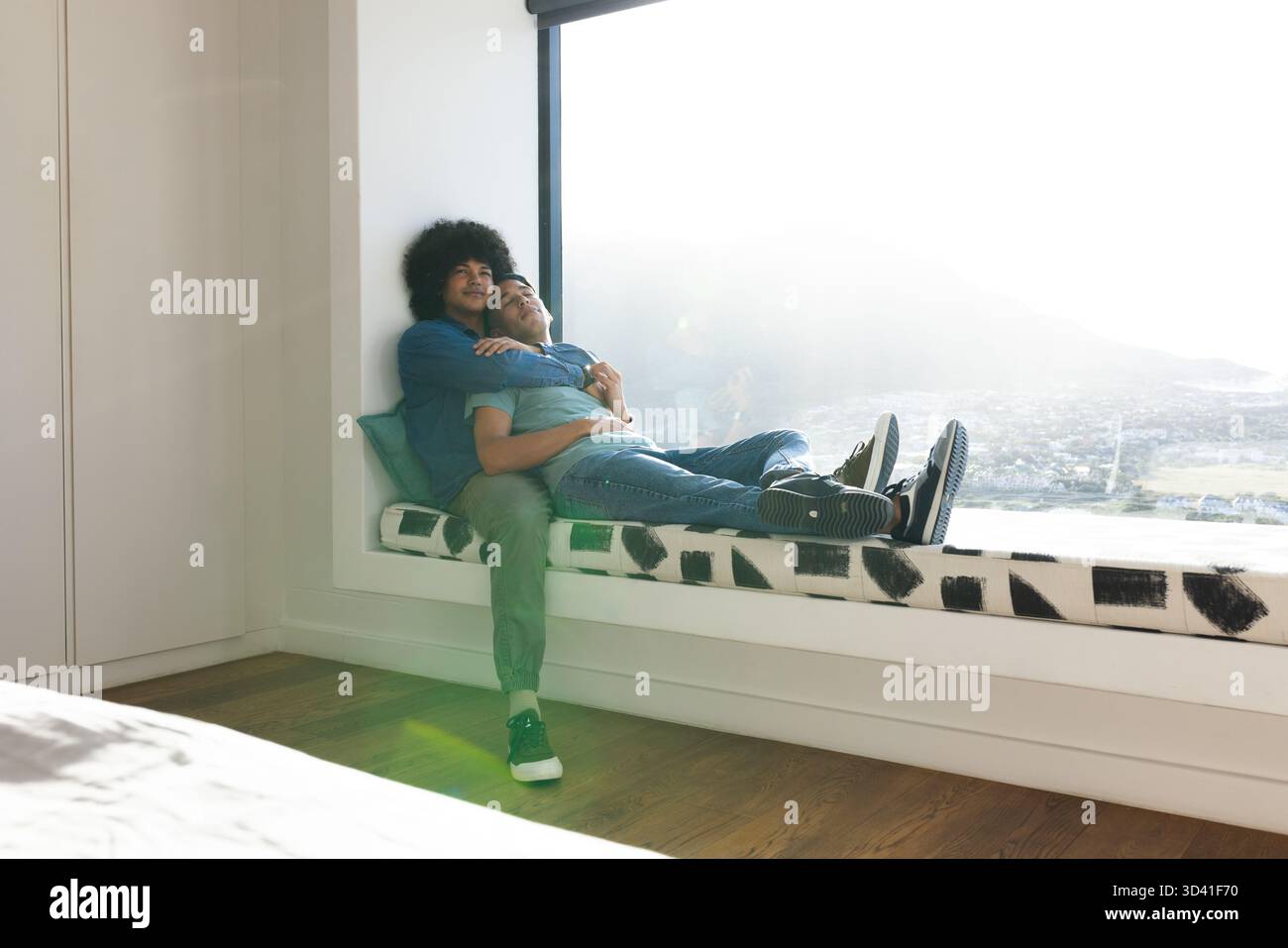 Câlin divers partenaires masculins assis sur le siège de fenêtre intégré à la maison, avec vue sur la ville Banque D'Images