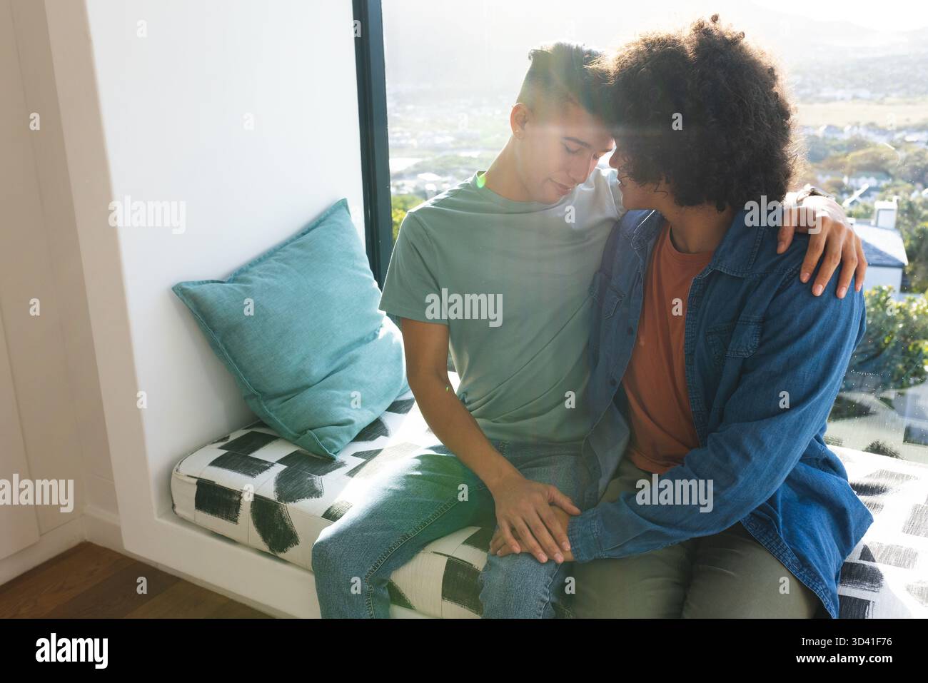 Penchant divers partenaires masculins câlins sur un banc de fenêtre intégré dans le coin fenêtre, avec oreiller sarcelle Banque D'Images