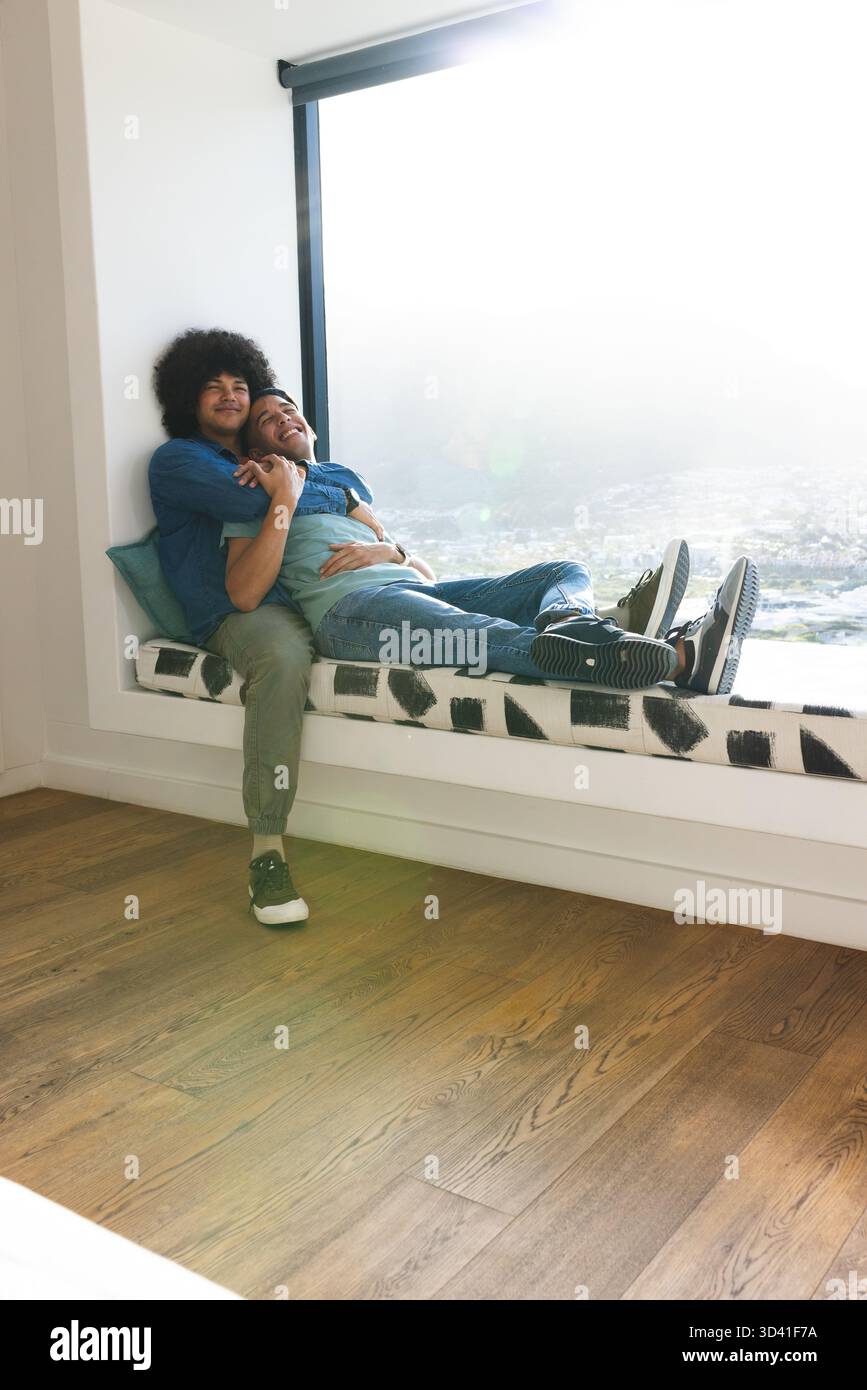 Embrassant divers partenaires masculins assis sur le banc de fenêtre à la maison, avec oreiller de jet sarcelle Banque D'Images