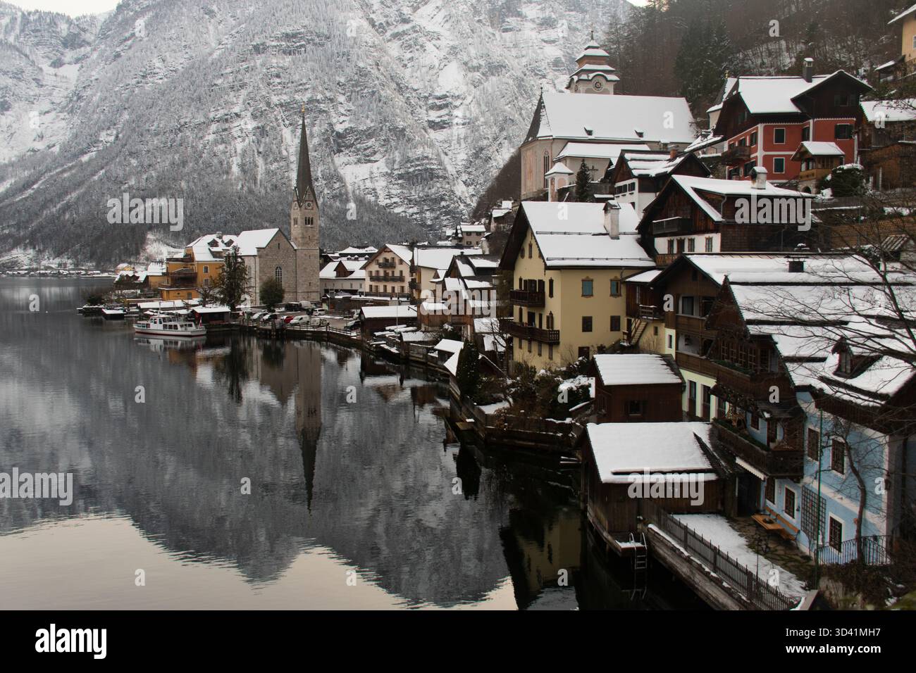 Vue panoramique hivernale classique de Hallstatt avec flèche d'église et maisons enneigées au bord du lac. Banque D'Images
