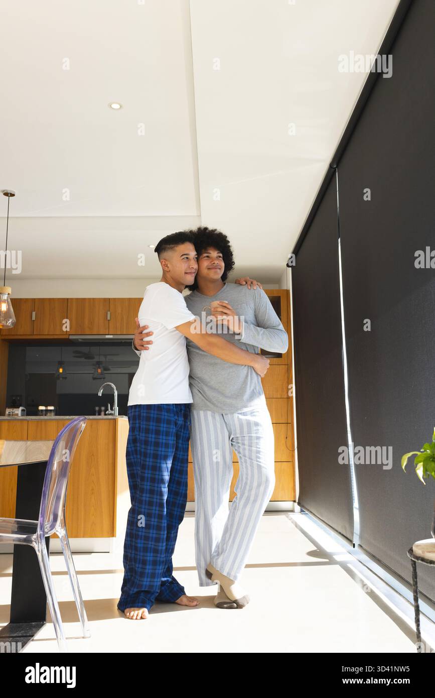 Embrassant divers couples masculins debout dans la cuisine moderne, avec tasse à café et lumières suspendues Banque D'Images