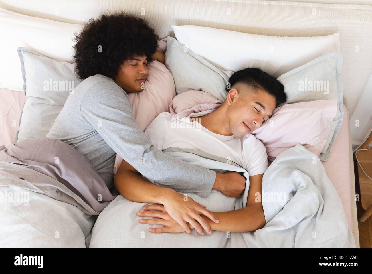 Couchage de deux hommes serrés sous une couette moelleuse dans la chambre, avec plusieurs oreillers contre la tête de lit Banque D'Images