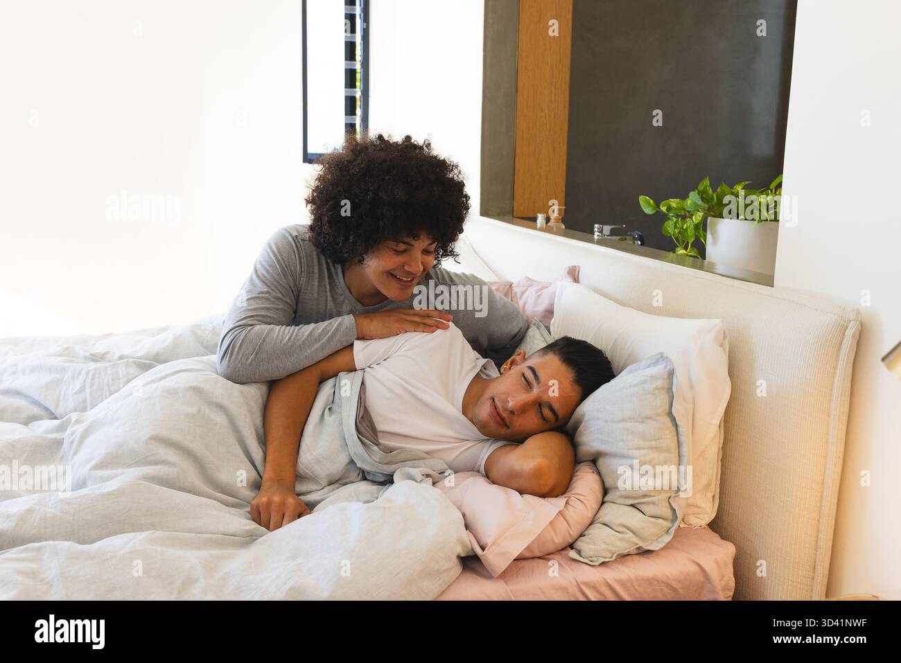 Repos divers partenaires masculins allongés sur le lit dans une chambre moderne, avec couette légère et plante en pot Banque D'Images